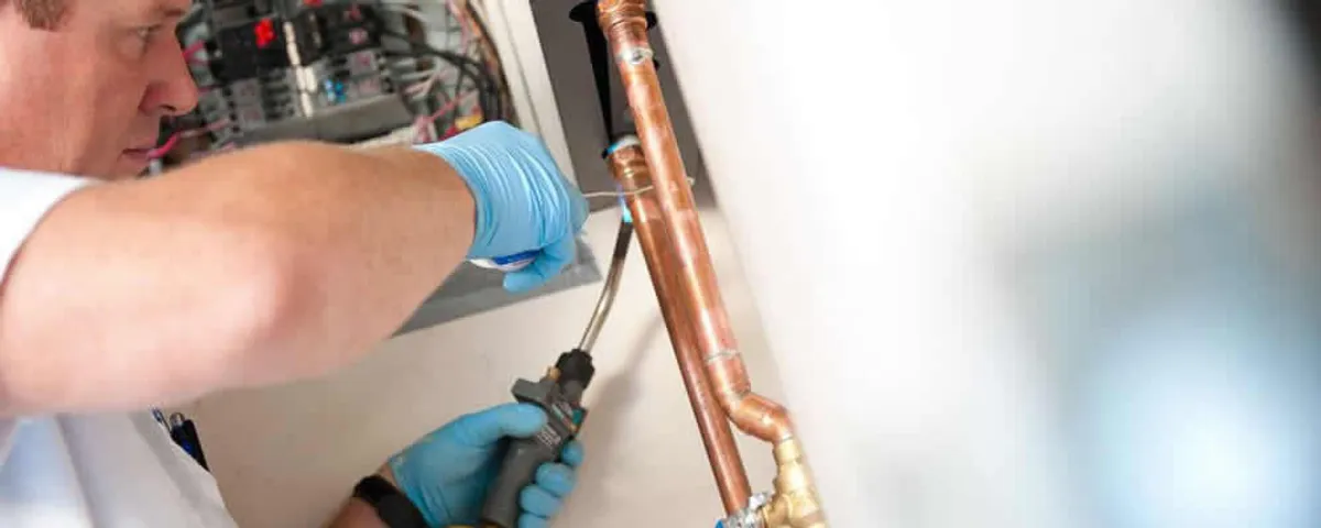 Water heater repair technician testing copper pipe connections and controls in Kansas City, KS